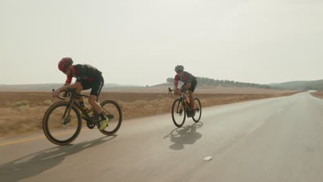 Cámara-Lenta-De-Dos-Profesionales-Ciclistas-De-Carretera-Montando-Rápido-En-La-Carretera-Vacía-Del-Desierto