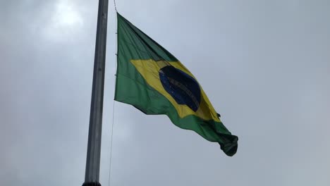 Brasilianische-Flagge-Auf-Der-Stange-Gehisst-Und-Winkend,-Auf-Bewölktem-Hintergrund