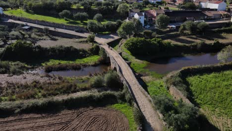 Un-Dron-Retrocede-Y-Se-Eleva-Sobre-El-Campo-De-Portugal-Junto-A-Un-Antiguo-Puente-Romano