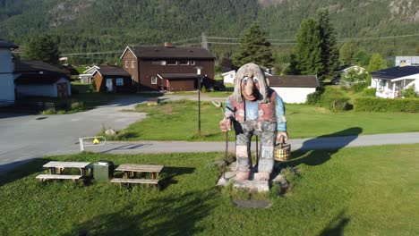 Norwegian-traditional-troll-statue-from-fairytales-standing-outdoor-at-Flaa-Hallingdal---Summer-sunset-with-long-shadows-and-houses-in-background