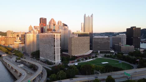 Aerial-view-of-traffic-on-Interstate-279,-with-sunset-lit-Pittsburgh-downtown-background---rising,-drone-shot