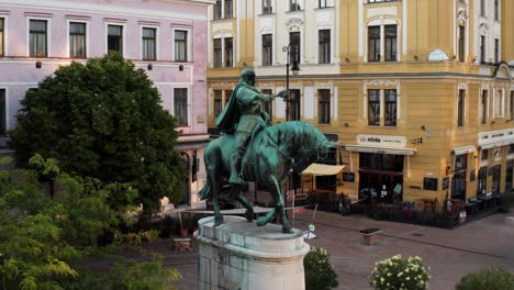 Equestrian-Statue-Of-Hunyadi-Janos-In-Pecs,-Hungary-With-Pecs-City-Hall-In-Background-On-An-Early-Morning