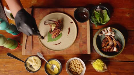 Top-down-view-of-a-sophisticated-professional-fine-dinning-chef-plating-the-smoked-octopus-and-drizzle-extra-virgin-olive-oil-to-complete-the-dish