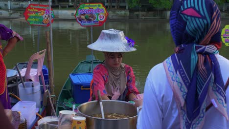 Thailändische-Frau-Mit-Traditionellem-Hut,-Die-Asiatische-Speisen-An-Den-Ufern-Des-Schwimmenden-Marktflusses-Klong-Hae-Verkauft