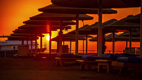 Sonnenaufgang-Im-Zeitraffer-Mit-Einer-Yacht,-Die-Hinter-Den-Sonnenschirmen-Am-ägyptischen-Roten-Meer-Verankert-Ist
