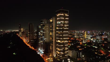 Ascending-drone-shot-of-Lighting-city-of-Santo-Domingo-at-night-with-high-rise-buildings