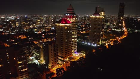 Vista-De-Drones-De-Los-Edificios-De-La-Torre-De-Iluminación-Y-El-Paisaje-Urbano-De-La-Ciudad-De-Santo-Domingo-Por-La-Noche