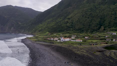 coastal-rural-village,-a-church-with-lush-green-cliffs-landscape,-Fajã-de-Santo-Cristo,-São-Jorge-island,-the-Azores,-Portugal