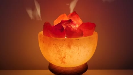 Himalayan-salt-lamp-glowing-on-а-table-against-dark-background,-spin,-close-up