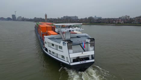 Luftparallaxe-Um-Das-Heck-Des-Scaldis-Containerschiffs-Geschossen,-Das-An-Einem-Bewölkten-Tag-In-Dordrecht-Entlang-Der-Oude-Maas-Fährt