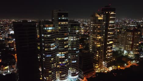 Drohne-Umkreist-Schuss-Von-Beleuchteten-Luxusturmgebäuden-An-Der-Avenida-Anacaona-Bei-Nacht,-Santo-Domingo