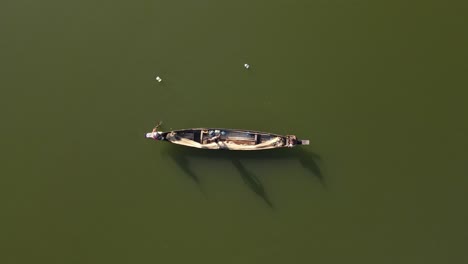 Top-down-aerial-shot-of-a-small-wooden-boat-in-a-lake-and-fishermen-catching-fish-with-net-in-traditional-style