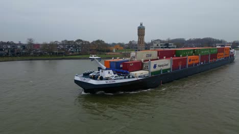 Aerial-Off-Port-Side-Of-Scaldis-Container-Ship-Travelling-Along-Oude-Maas-On-Overcast-Day-In-Dordrecht