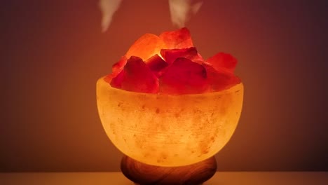 Himalayan-salt-lamp-glowing-on-а-table-against-dark-background,-rotating,-close-up