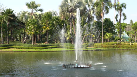 A-panning-view-of-a-fountain-spraying-water-in-a-pond-with-an-arched-bridge-in-the-background-surrounded-by-beautiful-plants
