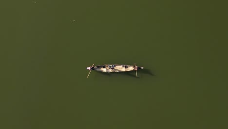 Top-down-aerial-shot-of-a-small-wooden-boat-in-a-lake-with-fishermen-on-board-catching-fish-using-fishing-net