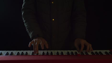 Close-up-front-view-of-an-elegantly-dressed-man-playing-the-piano-with-both-hands-in-a-darkened-room