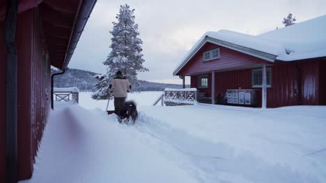 Man-Clearing-Backyard-In-Deep-Snow-Using-Sled-Shovel-In-Indre-Fosen,-Norway---wide