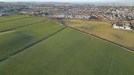 Aerial-view-of-a-green-field-with-a-road-and-a-great-city-in-the-background