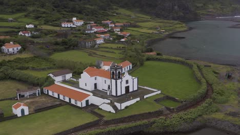 white-church-in-a-coastal-rural-village,-with-lush-green-landscape,-Fajã-de-Santo-Cristo,-São-Jorge-island,-the-Azores,-Portugal