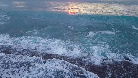 Pacific-ocean-sunset-on-the-west-shore-of-oahu-honolulu-hawaii-during-golden-hour-with-brilliant-shades-of-orange-yellow-and-blue-over-crashing-waves-and-seafoam,-AERIAL-TILT-UP-REVEAL