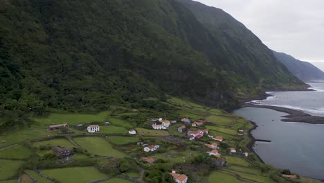 Drone-reveiling-view-of-a-coastal-village,-lush-green-cliffs-landscape,-Fajã-de-Santo-Cristo,-São-Jorge-island,-the-Azores,-Portugal