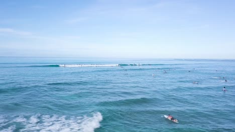 Surfistas-Atrapando-Olas-En-La-Hermosa-Playa-De-Waikiki-En-Honolulu-Hawaii-Cielo-Azul-Brillante,-Pan-De-Camiones-Aéreos