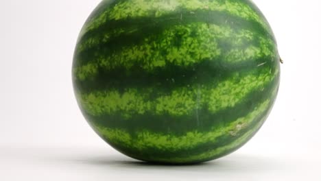 Whole,-ripe-green-striped-fresh-watermelon-being-dropped-onto-white-table-top-and-bouncing-up-and-down-in-slow-motion