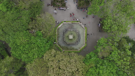 Top-down-aerial-footage-of-a-fountain-with-tourists-walking-around-in-the-main-square-in-Antigua,-Guatemala