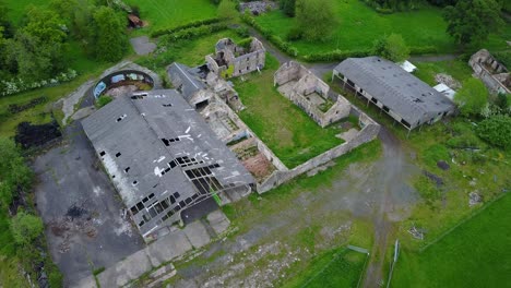 Aerial-footage-of-abandoned-farm-in-ruins-surrounded-by-green-fields-and-vegetation