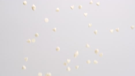 White-chocolate-chips-raining-down-on-white-backdrop-in-slow-motion