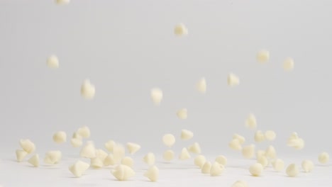 White-chocolate-chips-falling-and-bouncing-around-on-white-table-top-and-landing-in-a-pile-in-slow-motion