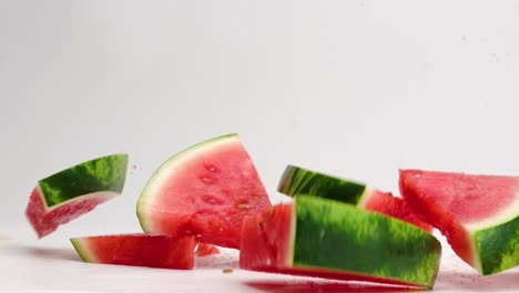 Fresh,-bright-pink-watermelon-sliced-wedges-with-green-rind-falling-onto-white-table-top-with-juice-droplets-spraying-in-slow-motion