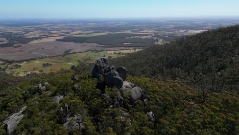 Aerial-orbit-of-boulder-lookout-in-Australian-bush,-farmland-in-background