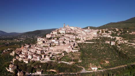 Paisaje-Aéreo-De-La-Ciudad-Medieval-De-Trevi-En-La-Cima-De-Una-Colina-Verde,-Italia