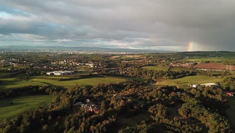 Aerial-video-with-the-rainbow-in-a-cloudy-sky-flying-over-some-fields-and-city