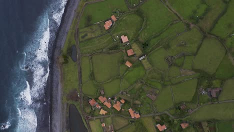 top-down-panorama-view-of-a-coastal-village-lush-green-landscape,-Fajã-de-Santo-Cristo,-São-Jorge-island,-the-Azores,-Portugal