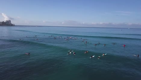 Eine-Große-Menge-Surfer-Warten-Auf-Eine-Welle-Auf-Dem-Wasser-Am-Strand-Von-Waikiki-In-Honolulu-Hawaii,-Aerial-Trucking-Pan