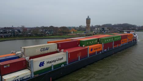Aerial-Off-Port-Side-Of-Scaldis-Container-Ship-Navigating-Past-Along-Oude-Maas-On-Overcast-Day-In-Dordrecht