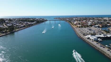 Aerial-of-boats-in-channel-of-water-and-cars-driving-over-bridge-in-background