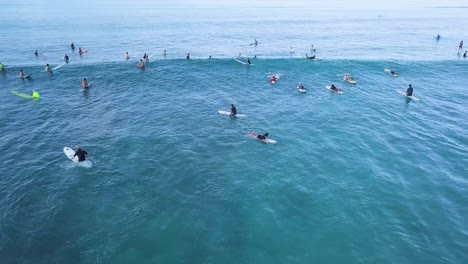 Aerial-of-lots-of-surfers-waiting-for-waves-at-Waikiki-Beach-Honolulu-Hawaii-in-bright-blue-water,-AERIAL-ORBIT
