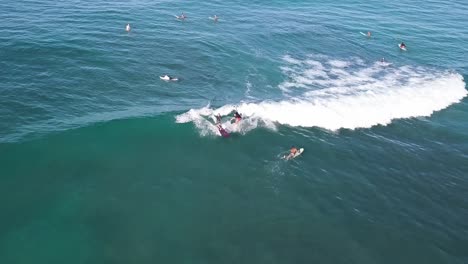 Two-surfers-sharing-a-wave-on-waikiki-beach-in-honolulu-hawaii-with-crystal-blue-water-and-other-surfers-surrounding-them,-AERIAL-DOLLY