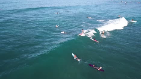 Three-surfers-catching-a-medium-sized-wave-on-waikiki-beach-in-honolulu-hawaii-on-a-beautiful-day,-AERIAL-DOLLY-PULLBACK