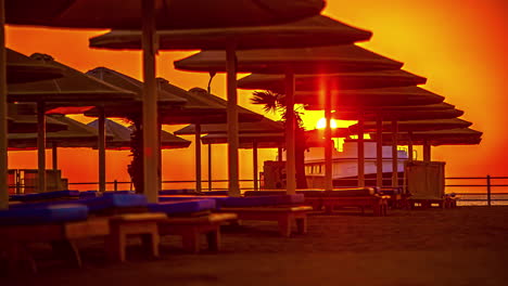 Sonnenschirm-Und-Leere-Liegestühle-Bei-Sonnenuntergang-Mit-Ankommendem-Und-Abfahrendem-Boot-Im-Hintergrund