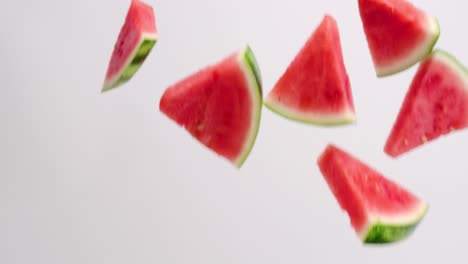 Fresh,-bright-pink-watermelon-sliced-wedges-with-green-rind-raining-down-on-white-backdrop-in-slow-motion