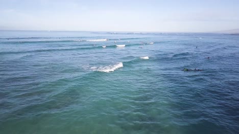 Waves-aggressively-crashing-over-surfers-on-waikiki-beach-honolulu-hawaii,-AERIAL-DOLLY-TILT-DOWN