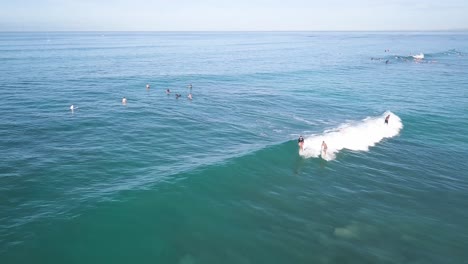 Surfers-riding-a-wave-at-Waikiki-Beach-Honolulu-Hawaii-on-a-blue-sky-day,-AERIAL-DOLLY