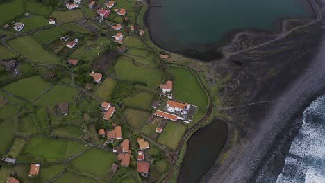 Drone-top-down-boom-view-of-a-coastal-village-lush-green-landscape,-Fajã-de-Santo-Cristo,-São-Jorge-island,-the-Azores,-Portugal
