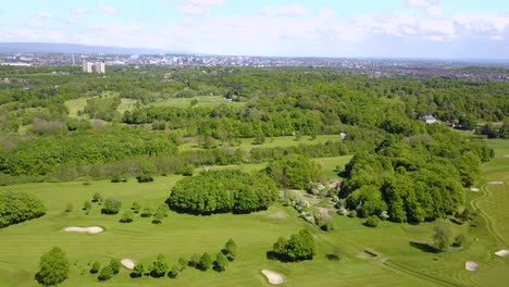Aerial-video-of-a-lush-golf-course-surrounded-by-green-fields-and-trees-with-a-city-skyline-in-the-distance