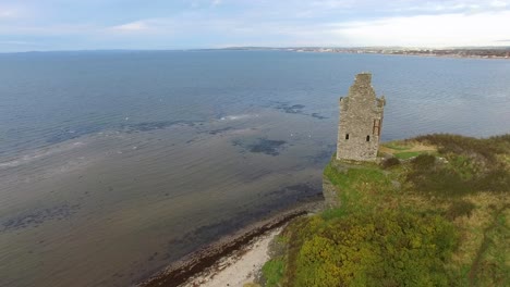 Aerial-top-up-video-of-a-ruined-stone-tower-on-the-edge-of-a-cliff-above-the-water-and-the-horizon-in-the-background